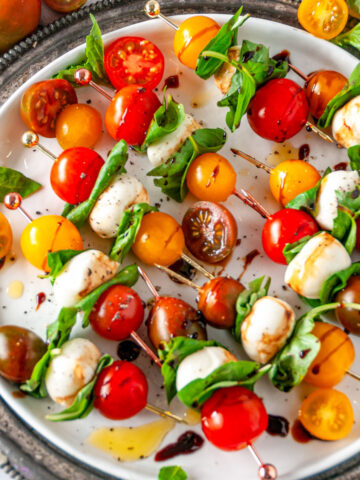 Caprese Salad Bites with heirloom cherry tomatoes, mozzarella balls, and fresh basil skewers on white plate with gray platter