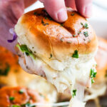 One Pan Turkey Swiss Cheese Melt Sliders held in hand lifted with long piece of cheese melting above sheet pan