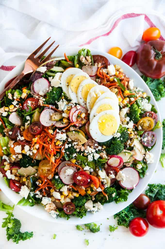 Loaded Chopped Veggie Salad in white bowl with copper fork and tomatoes