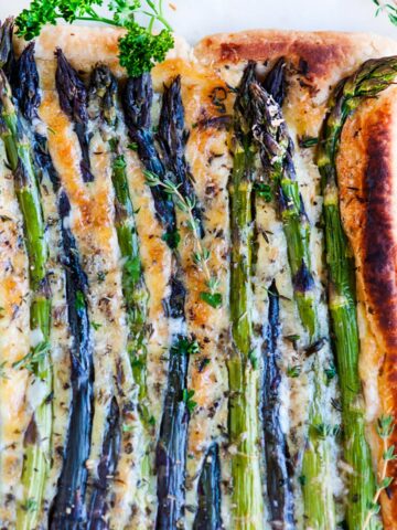 Spring Asparagus Brie Tart with fresh herbs on white marble overhead view