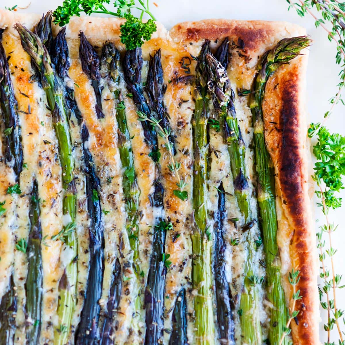 Spring Asparagus Brie Tart with fresh herbs on white marble overhead view