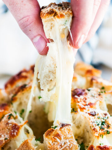 Cheesy Garlic Herb Pull Apart Bread sliced with cheesy piece pulled out by hand