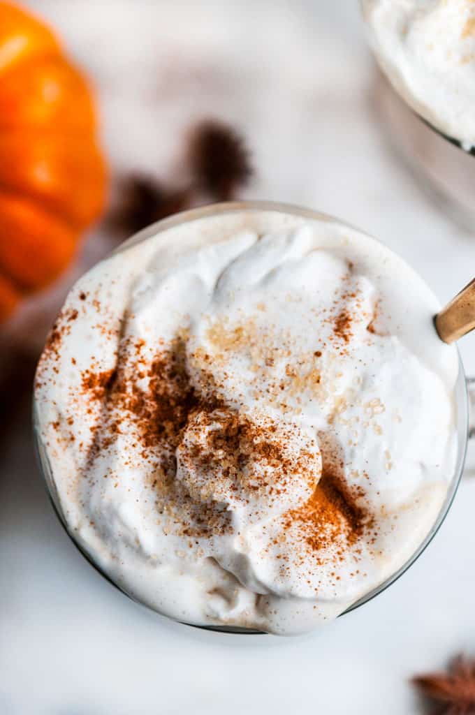 Pumpkin Spice Chai Latte in glass mug with whipped cream on and gold spoon on white marble