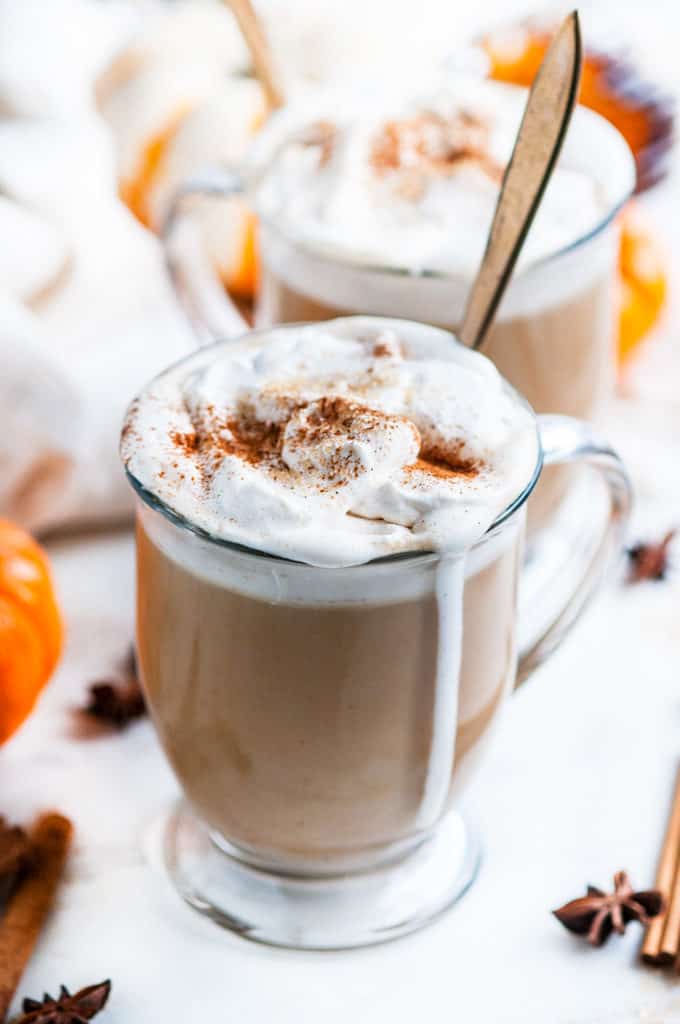 Pumpkin Spice Chai Latte in glass mugs with whipped cream on and gold spoon on white marble