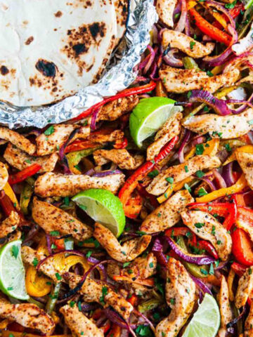 Sheet Pan Chicken Fajitas on sheet pan with tortillas in foil on white marble overhead view