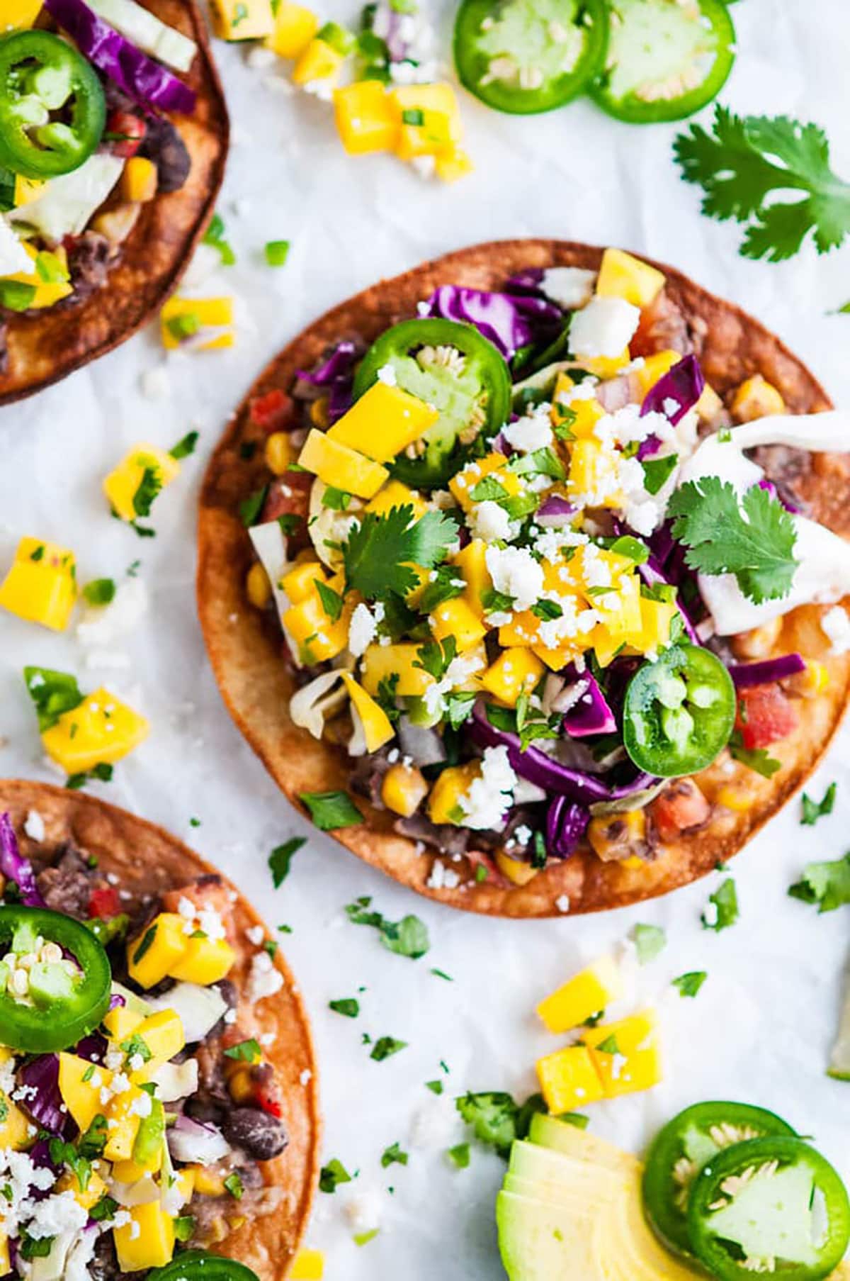 Vegetarian Black Bean Tostadas with Cabbage Slaw and Mango Salsa on white parchment paper overhead view