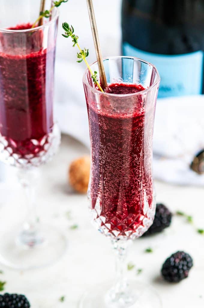 Blackberry bellini in champagne flutes with thyme and a bottle of prosecco