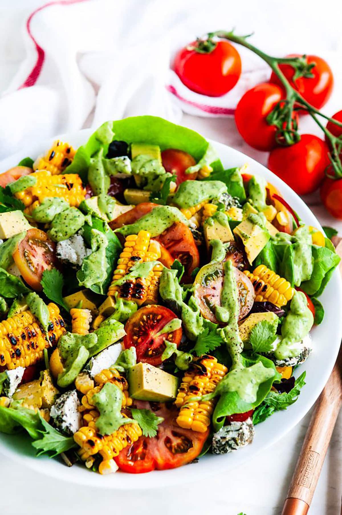 Grilled Corn Tomato Salad with Cilantro Avocado Dressing in a white bowl with serving tongs