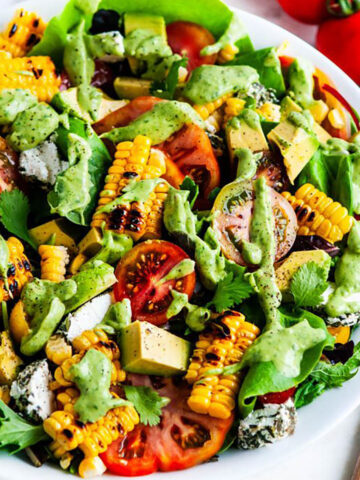 Grilled Corn Tomato Salad with Cilantro Avocado Dressing in a white bowl with serving tongs