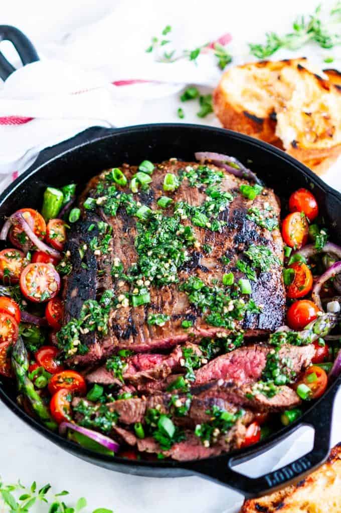Skillet flank steak in cast iron skillet with tomatoes, asparagus, and grilled bread 