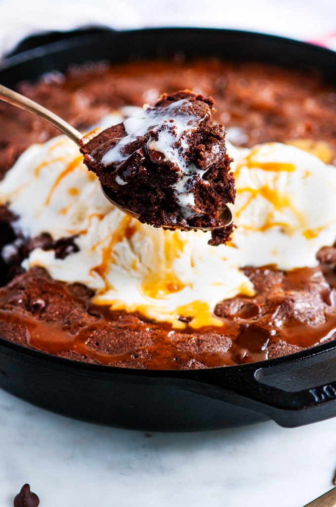 Chocolate Caramel Skillet Brownie in lodge cast iron skillet with vanilla ice cream scoop in gold spoon close up