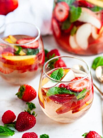 Peach Strawberry White Wine Sangria in wine glasses with gold spoons and fruit