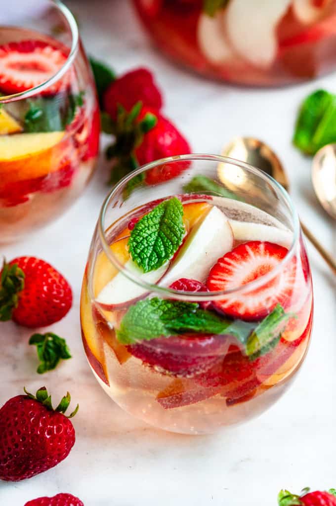 Peach Strawberry White Wine Sangria in wine glasses with gold spoons and fruit