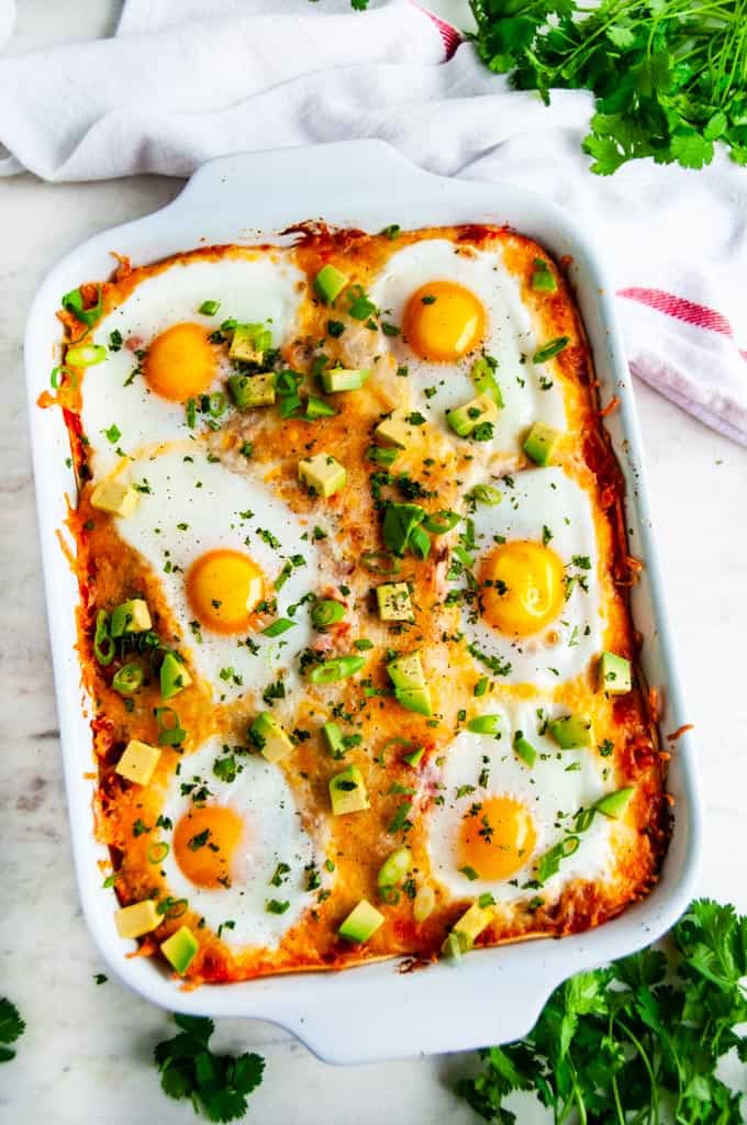 Cheesy Baked Huevos Rancheros Casserole in red dish with towel and cilantro