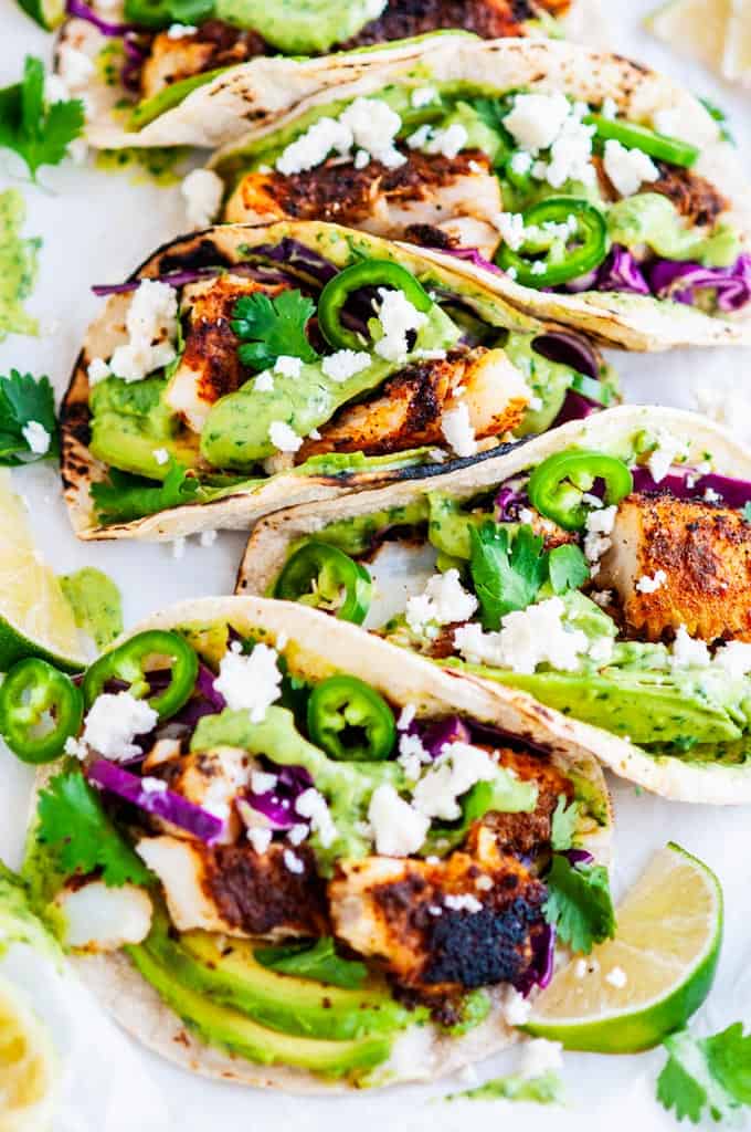 Blackened Cod Fish Tacos with Cilantro Avocado Sauce and limes on parchment paper