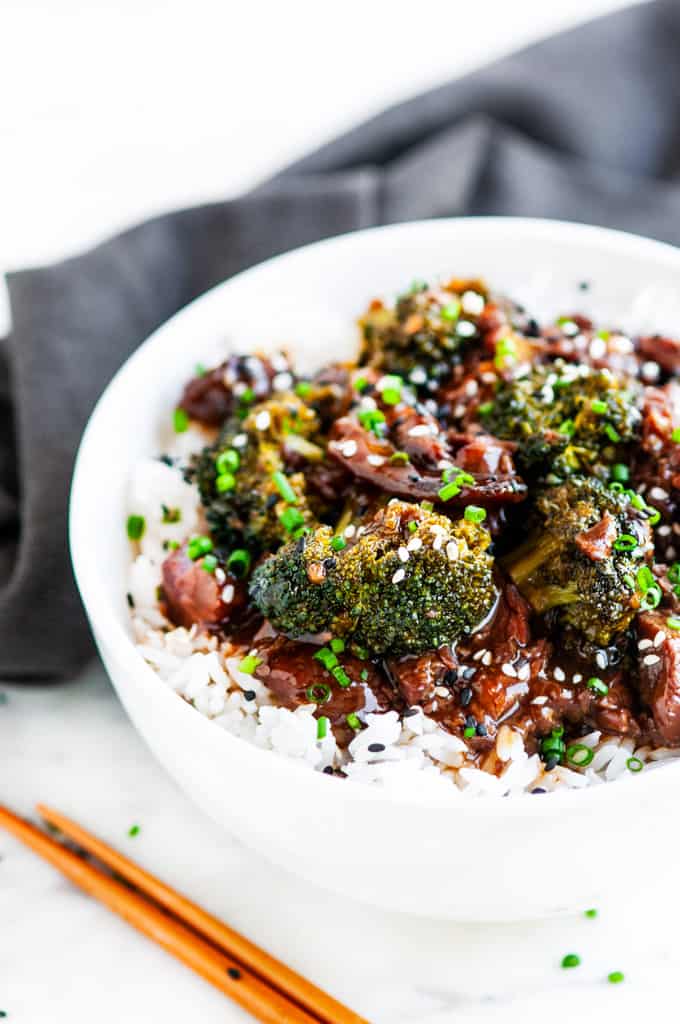 Slow Cooker Beef and Broccoli in white bowl with gray towel and chopsticks