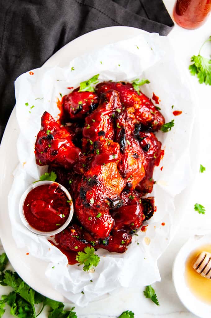 Baked Honey BBQ Chicken Wings on parchment with cilantro honey and bbq sauce