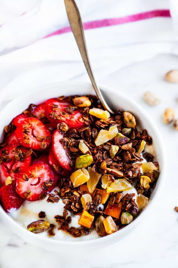 Pistachio Mango Granola white bowl strawberries and honey with a gold spoon