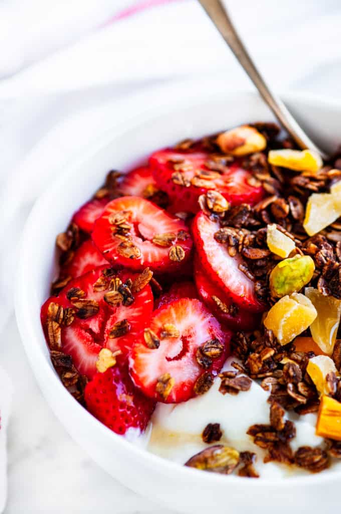 Pistachio Mango Granola white bowl strawberries and honey with a gold spoon
