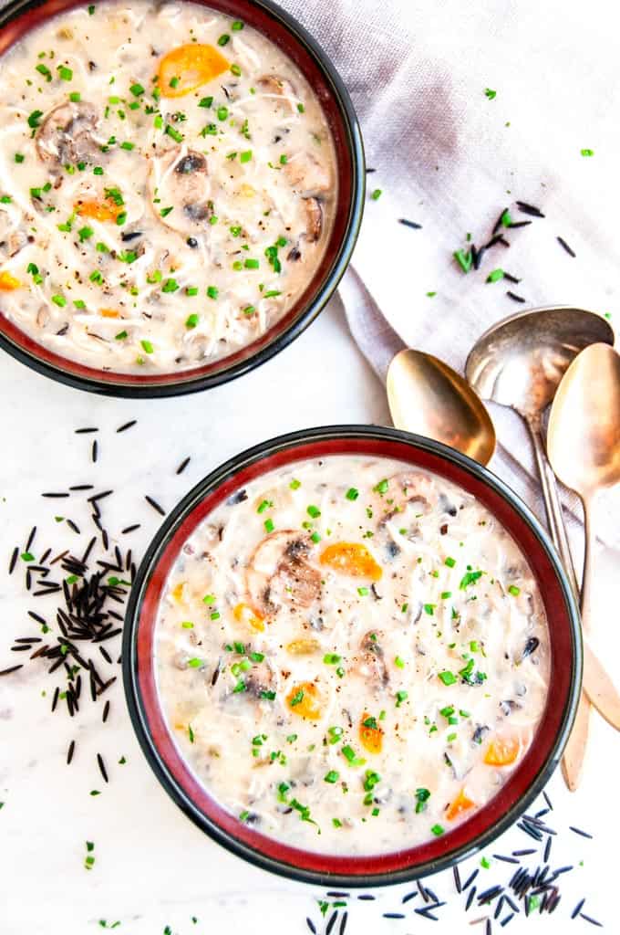 Slow Cooker Chicken Mushroom Wild Rice Soup in black and red bowls with gold spoons and silver ladle