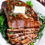 beef brisket sliced with butter and herbs on white platter