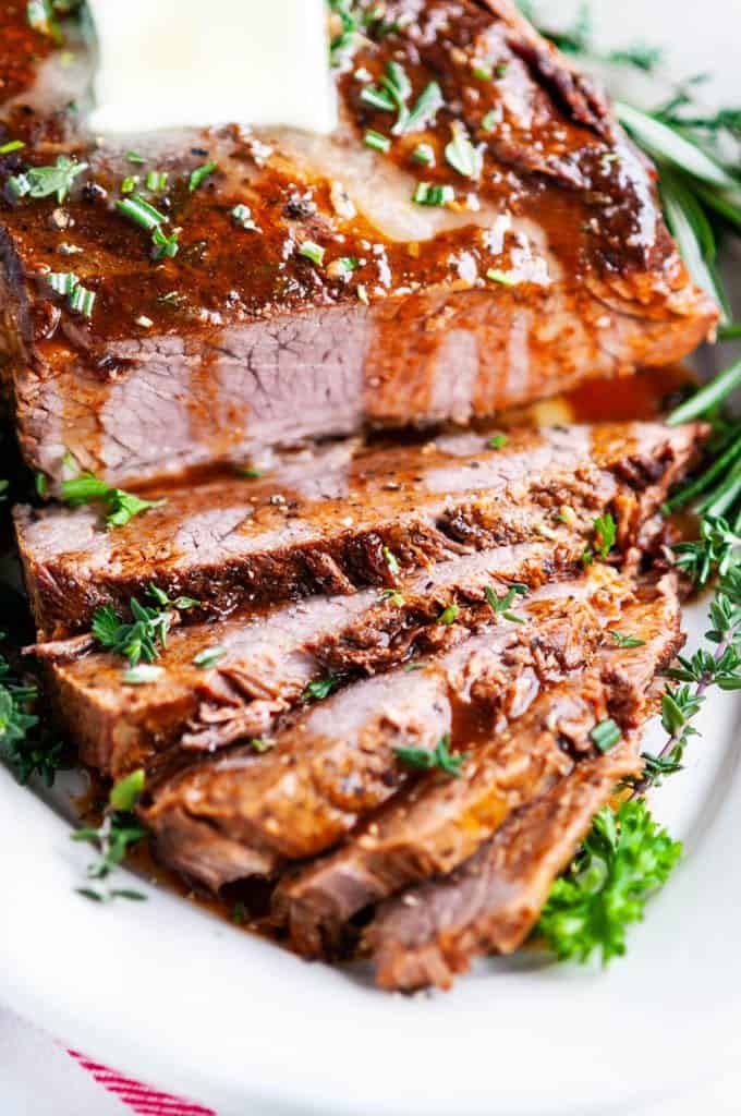 beef brisket sliced with butter and herbs on white platter