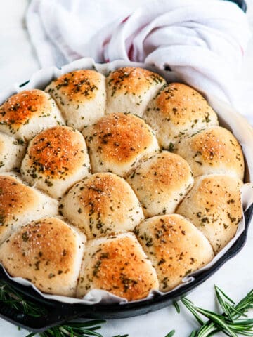 Rosemary Garlic Dinner Rolls in lodge cast iron skillet with parchment paper and white towel