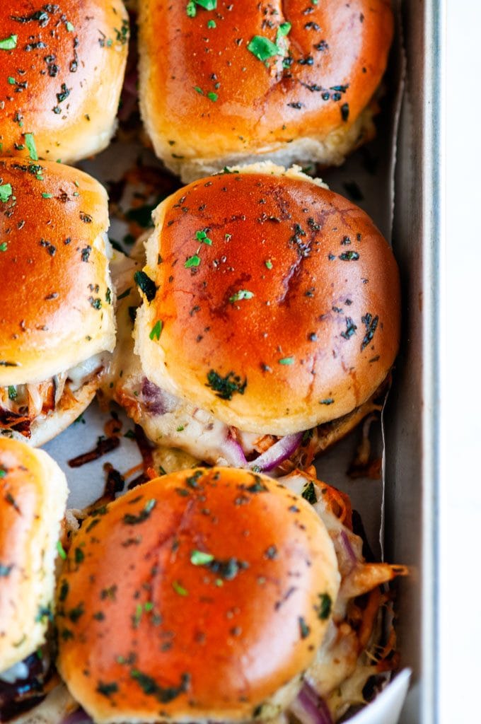 BBQ chicken sliders in gray baking pan on marble with parchment paper