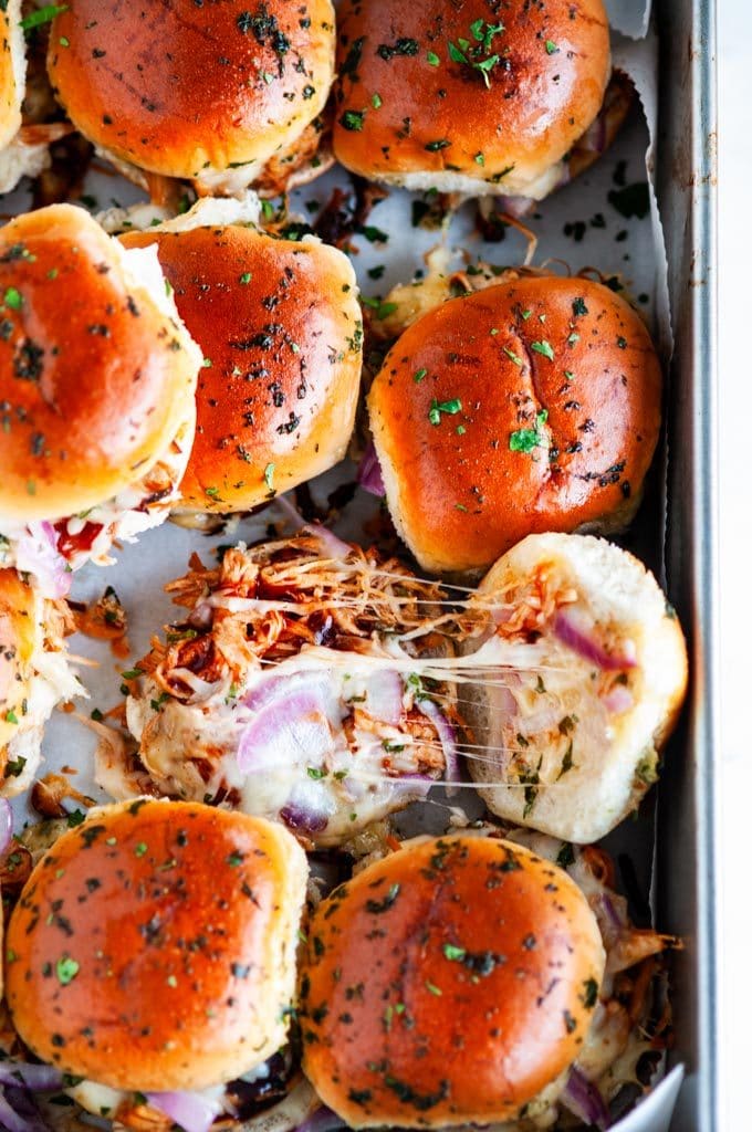 BBQ chicken sliders in gray baking pan on marble with parchment paper