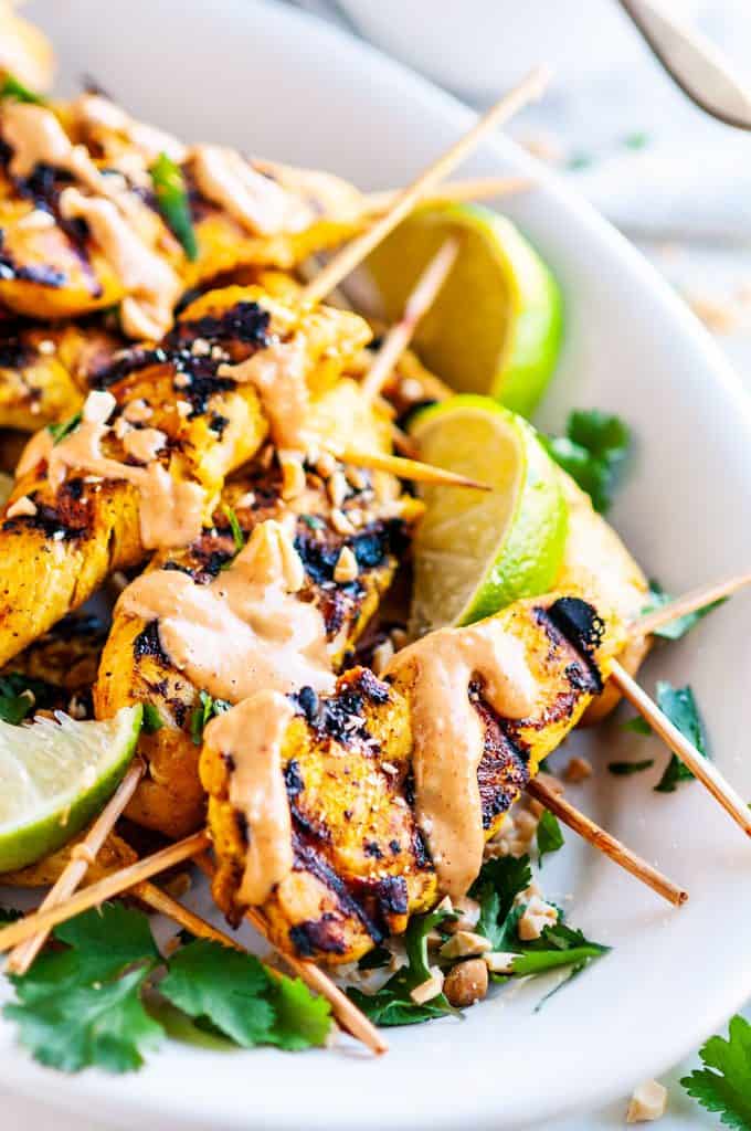 Chicken Satay Skewers with Peanut Sauce on white platter with limes and cilantro