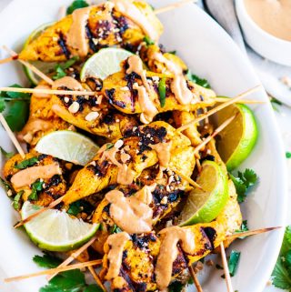Chicken Satay Skewers with Peanut Sauce on white platter with limes and cilantro