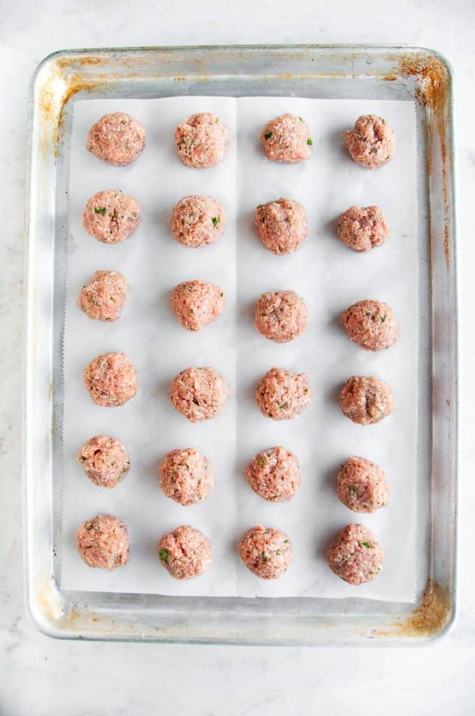 Baked Turkey Meatballs raw on sheet pan with parchment paper and white marble