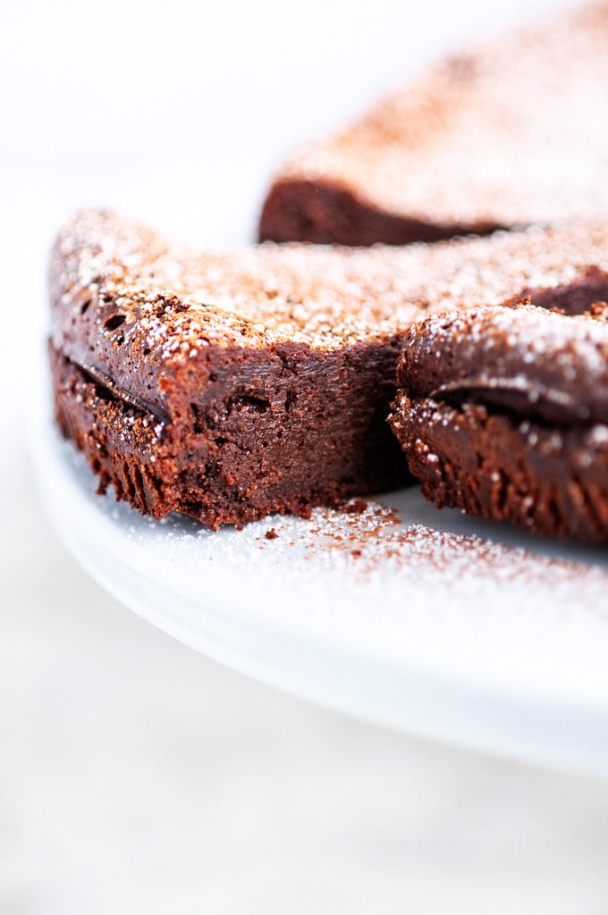 Flourless Chocolate Torte dusted with cocoa powder and powdered sugar on white marble