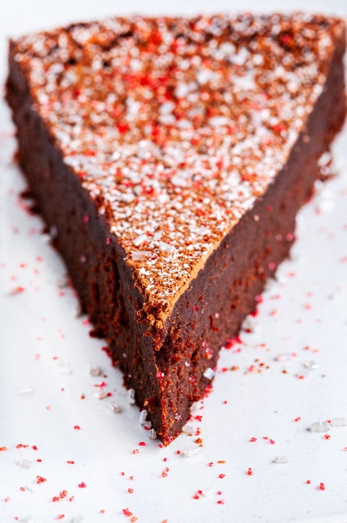 Flourless Chocolate Torte slice dusted with cocoa powder and powdered sugar on white marble