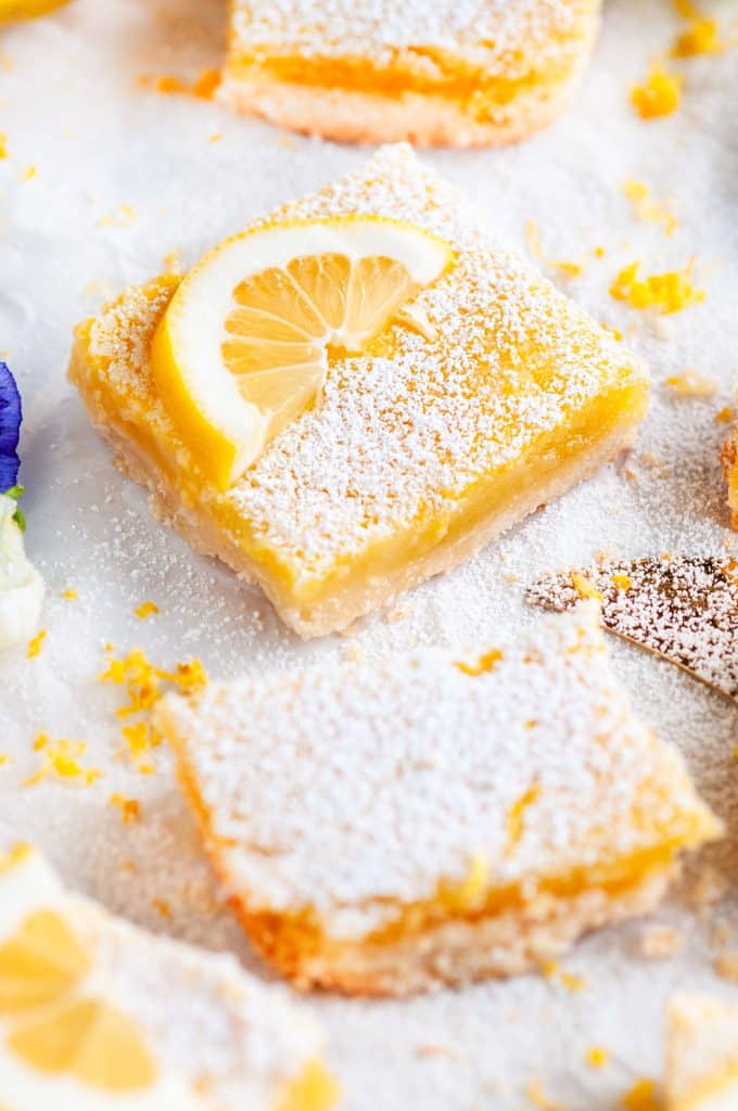 Best Ever Classic Lemon Bars with gold pie server and edible purple and white flowers close up