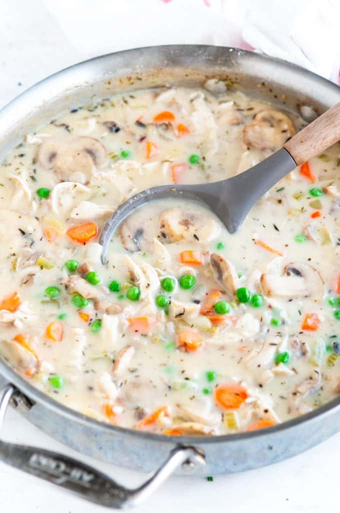 Chicken wild rice pot pie filling in all clad skillet with gray and wood mixing spoon
