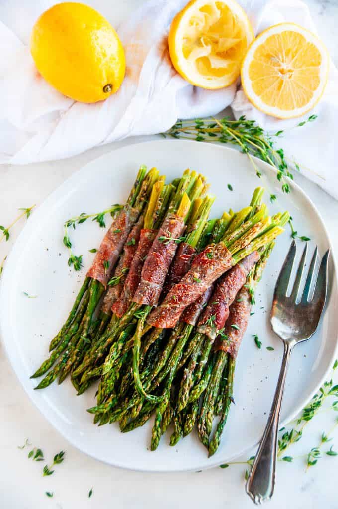 Garlic Parmesan Prosciutto Wrapped Asparagus on light gray plate with antique silver fork