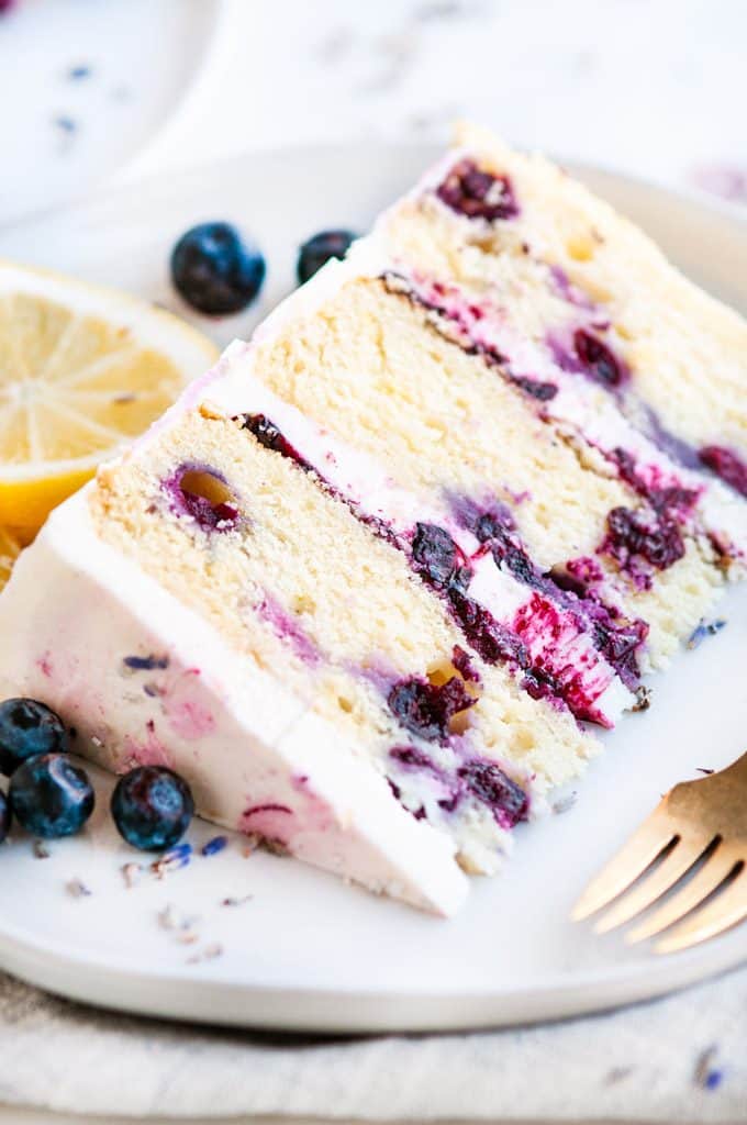 Lemon Blueberry Lavender Cake with Mascarpone Buttercream Frosting slice on white plate with gold fork