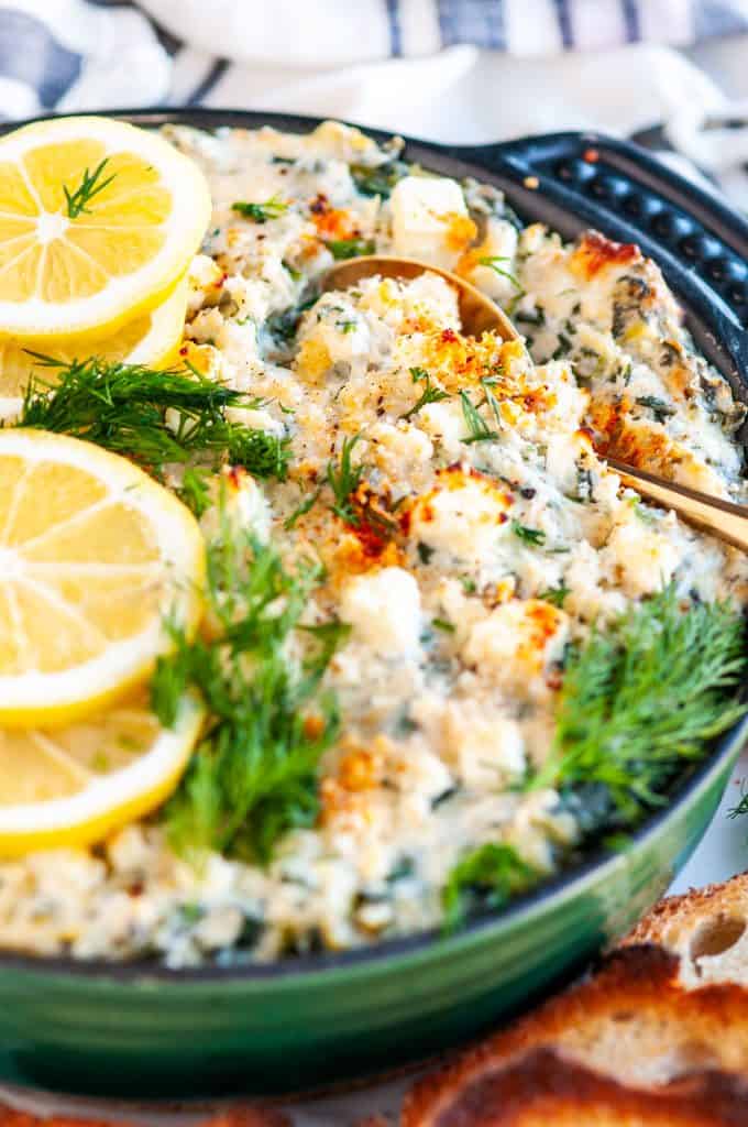 Lemon Spinach Artichoke Dip in blue cast iron dish with fresh dill, toasted baguette slices and gold serving spoon