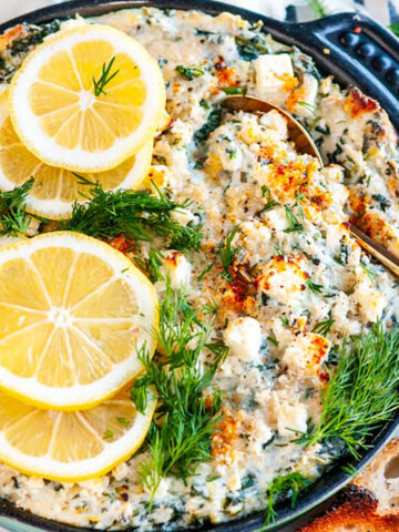 Lemon Spinach Artichoke Dip in blue cast iron dish with fresh dill, toasted baguette slices and gold serving spoon