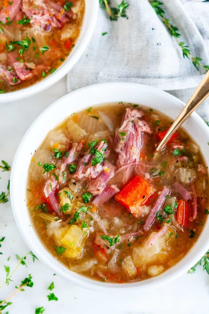 Slow Cooker Corned Beef and Cabbage Stew in white bowls with gold spoon and gray tea towel