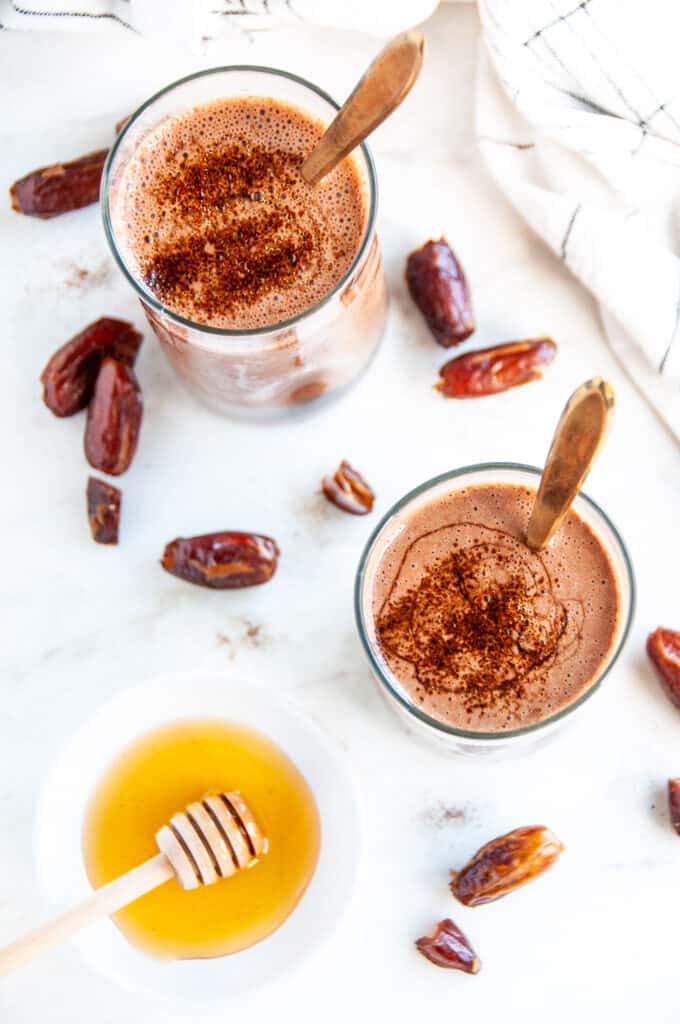 Dark Chocolate Date Smoothie with honey and gold spoons on white marble