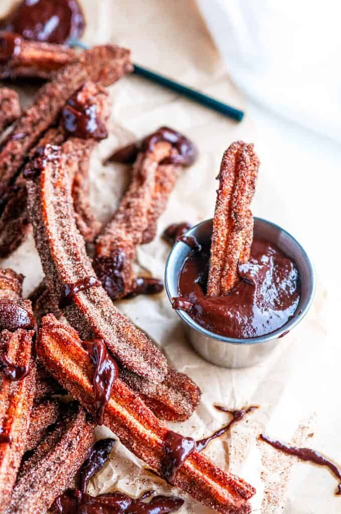 Homemade Churros with Mexican Dipping Sauce on brown parchment paper with metal tin and black spoon