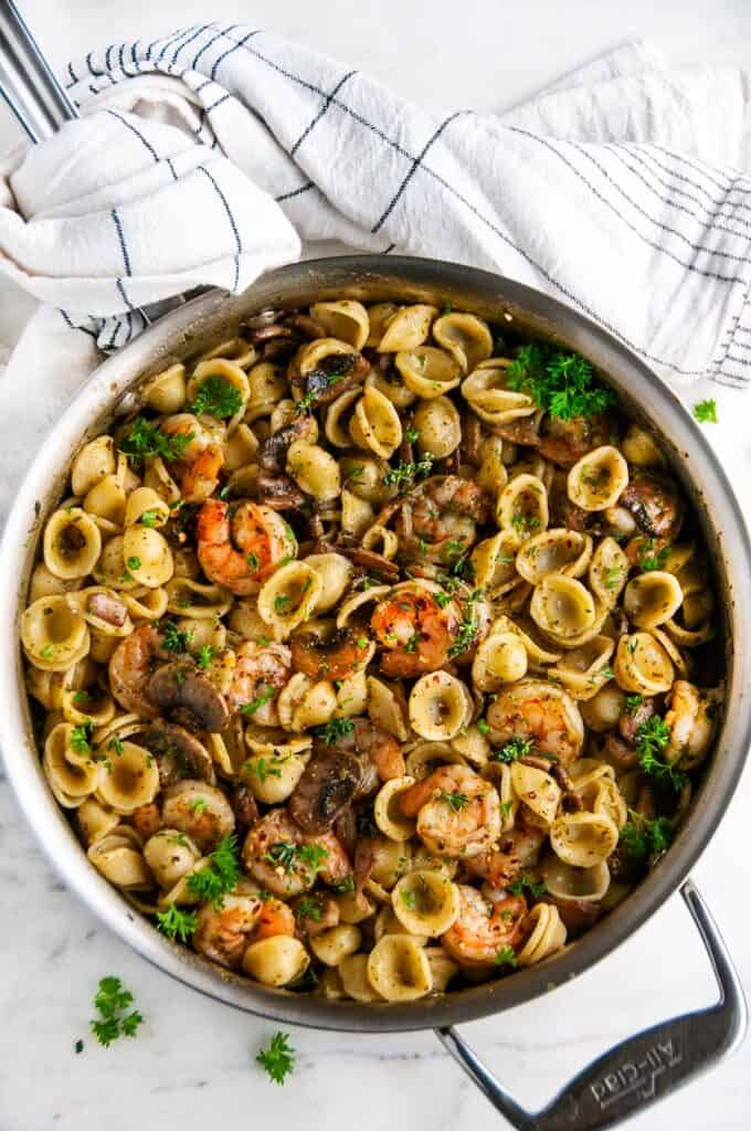 Quick and Easy Pesto Shrimp Pasta in all clad skillet with tea towel on white marble