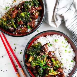 Skillet Beef and Broccoli in black and red bowls on marble with chopsticks and tea towel