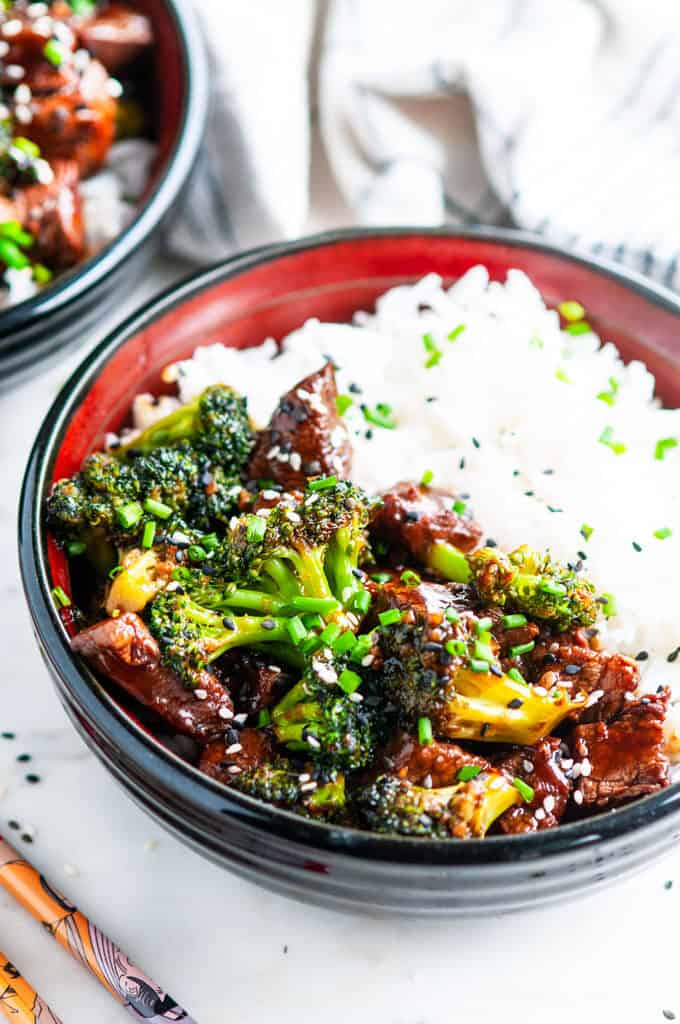 Skillet Beef and Broccoli in black and red bowls on marble with chopsticks and tea towel