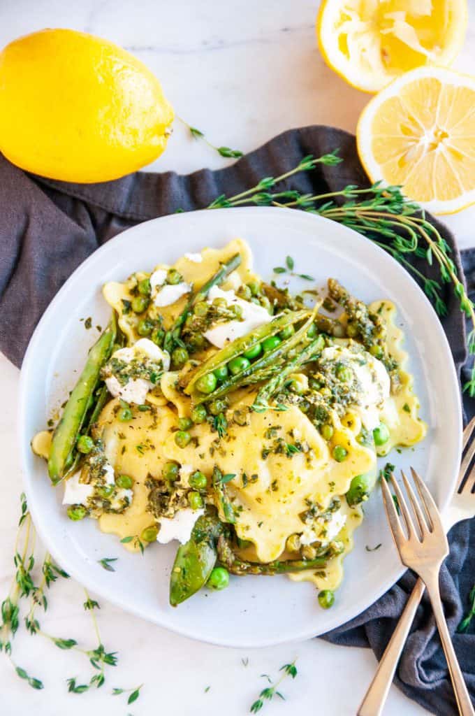 Spring Pea Asparagus Ricotta Ravioli on gray plate with lemons and gold fork
