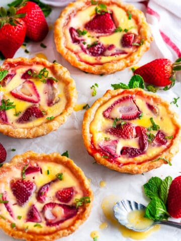 Strawberry Custard Honey Tarts with Lemon Curd on parchment paper with fresh mint