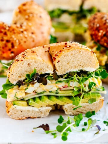 Avocado Egg Salad Bagel Sandwich half on parchment and white marble