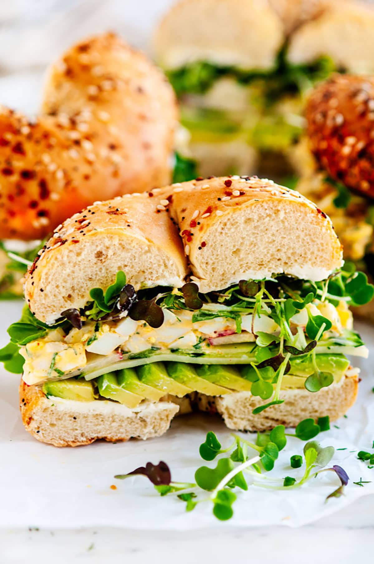 Avocado Egg Salad Bagel Sandwich half on parchment and white marble side view